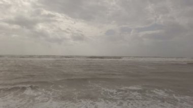 Stormy evening at the beach with rough sea splashing on the shore, a lot of foam water,  and overcast sky with dramatic light