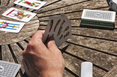 Turin, Italy - May 15, 2014: During coffee break, the employees play Trump with typical Neapolitan cards on a wooden table, first-person view on the game scene clipart