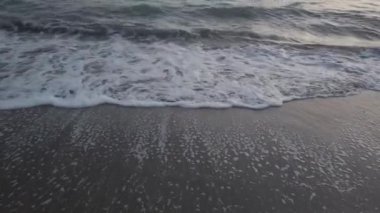 Kıyıya vuran okyanus dalgalarının alçak açılı görüntüsü koyu kum, bol köpük ve yeşil zümrüt renkli su.