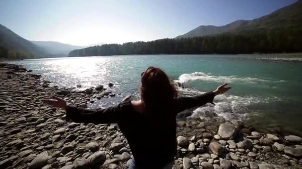 Ung kvinna sprida sina armar på stranden av floden turkos berg — Stockvideo