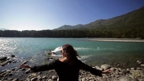 Junge Frau breitet ihre Arme am Ufer des türkisfarbenen Gebirgsflusses aus — Stockvideo