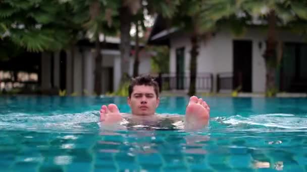 Egy fiatal férfi a szálloda medencéjében hátrahúzódás le, és az arc darabos — Stock videók