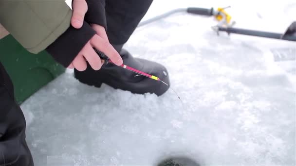 Un uomo seduto sul ghiaccio e a pescare. nelle mani della canna da pesca — Video Stock