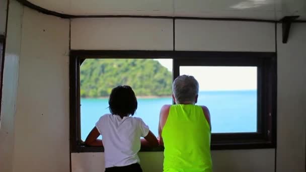 Abuelo y una mujer tailandesa en un ferry de carga están mirando por la ventana al mar — Vídeo de stock