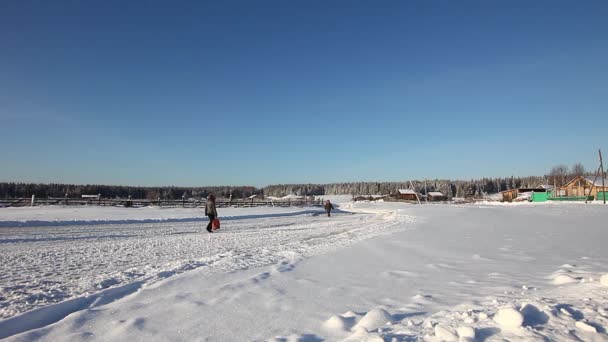 Två människor går på en snöig väg i byn — Stockvideo