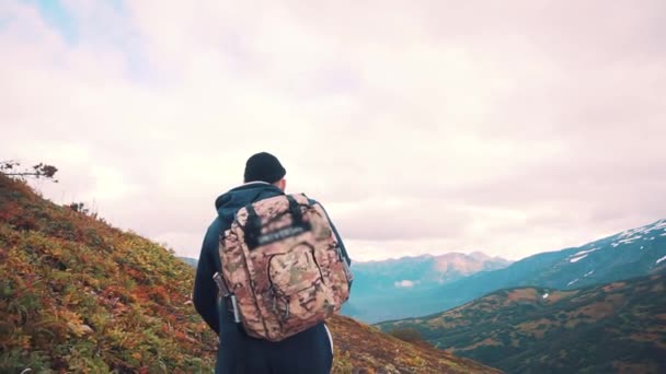 Egy hátizsák az egyik vállán magabiztosan mászik fel a hegy tetejére. — Stock videók