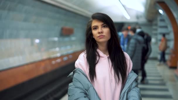 Jovencita se para esperando el tren en la estación de metro, muestra una cogida y se ríe — Vídeos de Stock