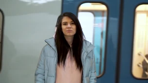 Genç bir kız geçen bir metro treninin önünde duruyor ve kameraya bakıyor.. — Stok video