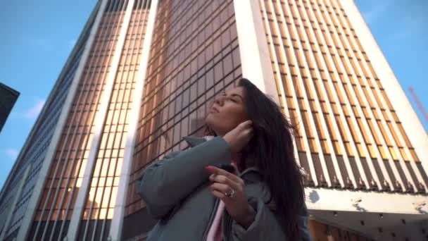 Girl pulls out and puts on wireless headphones among the skyscrapers — Stockvideo