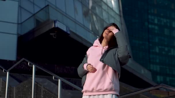 一个女孩站在一个现代化的建筑工地的后面，摩天大楼里摆弄着她的头发 — 图库视频影像