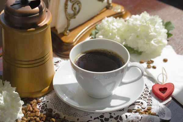Een beker met warme koffie tafel, koffie bonen en witte flowe — Stockfoto