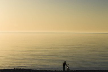 Bir çocuk sahilde günbatımı sırasında bir bisiklet ile.