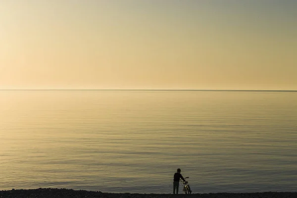 Un ragazzo con una bicicletta sulla spiaggia durante il tramonto . — Foto Stock