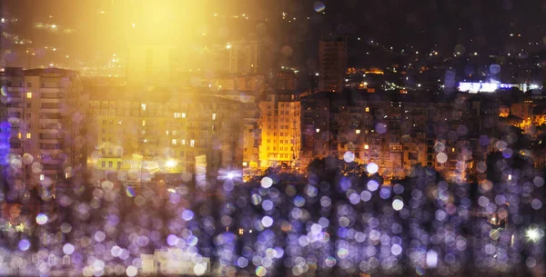 City in the rain at night. Window glass with raindrops defocused