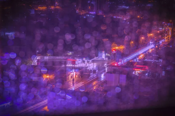 City in the rain at night. Window glass with raindrops defocused