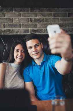 Çekici genç çift kafe restoranda iyi vakit geçiriyor. Bir cep telefonu tutan ve selfie yapma genç adam