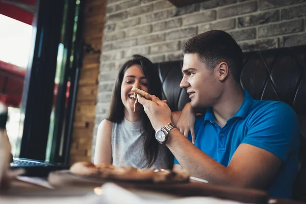 Çekici ve mutlu genç çift kafeteryada iyi vakit geçiriyor. Gülümsüyorlar ve pizza yiyorlar.