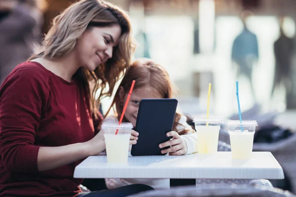 Mother and daughter sitting at cafe bar and looking something together at tablet