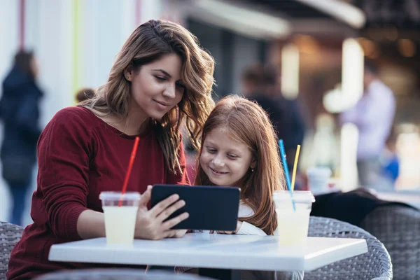 Mother and daughter sitting at cafe bar and looking something together at tablet