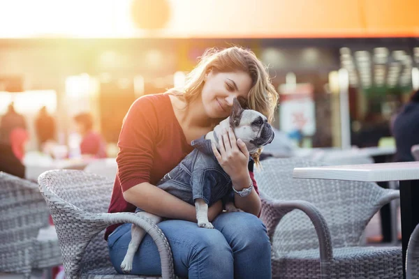 Kafe restoranda oturan ve çok güzel açık kahverengi Fransız buldozer tutan güzel ve genç birbayan. İnsanlar ve köpekler Tema