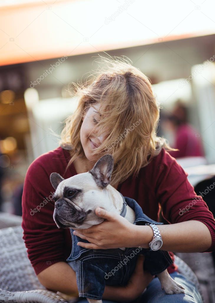 Beautiful young woman sitting in cafe restaurant and holding adorable fawn french bulldog. People and dogs theme