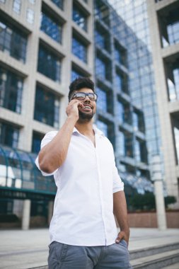 Büyük modern iş kurma gülümseyen ve cep telefonuyla konuşurken önünde duran genç Afro Amerikan yakışıklı