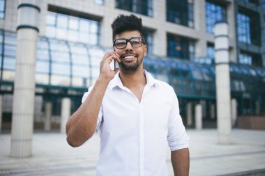 Büyük modern iş kurma gülümseyen ve cep telefonuyla konuşurken önünde duran genç Afro Amerikan yakışıklı