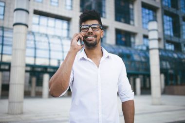 Büyük modern iş kurma gülümseyen ve cep telefonuyla konuşurken önünde duran genç Afro Amerikan yakışıklı