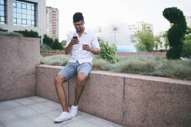 Büyük modern iş gülümseyen ve smartphone kullanarak bina önünde duran genç Afro Amerikan yakışıklı