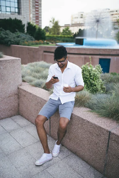 Büyük modern iş gülümseyen ve smartphone kullanarak bina önünde duran genç Afro Amerikan yakışıklı