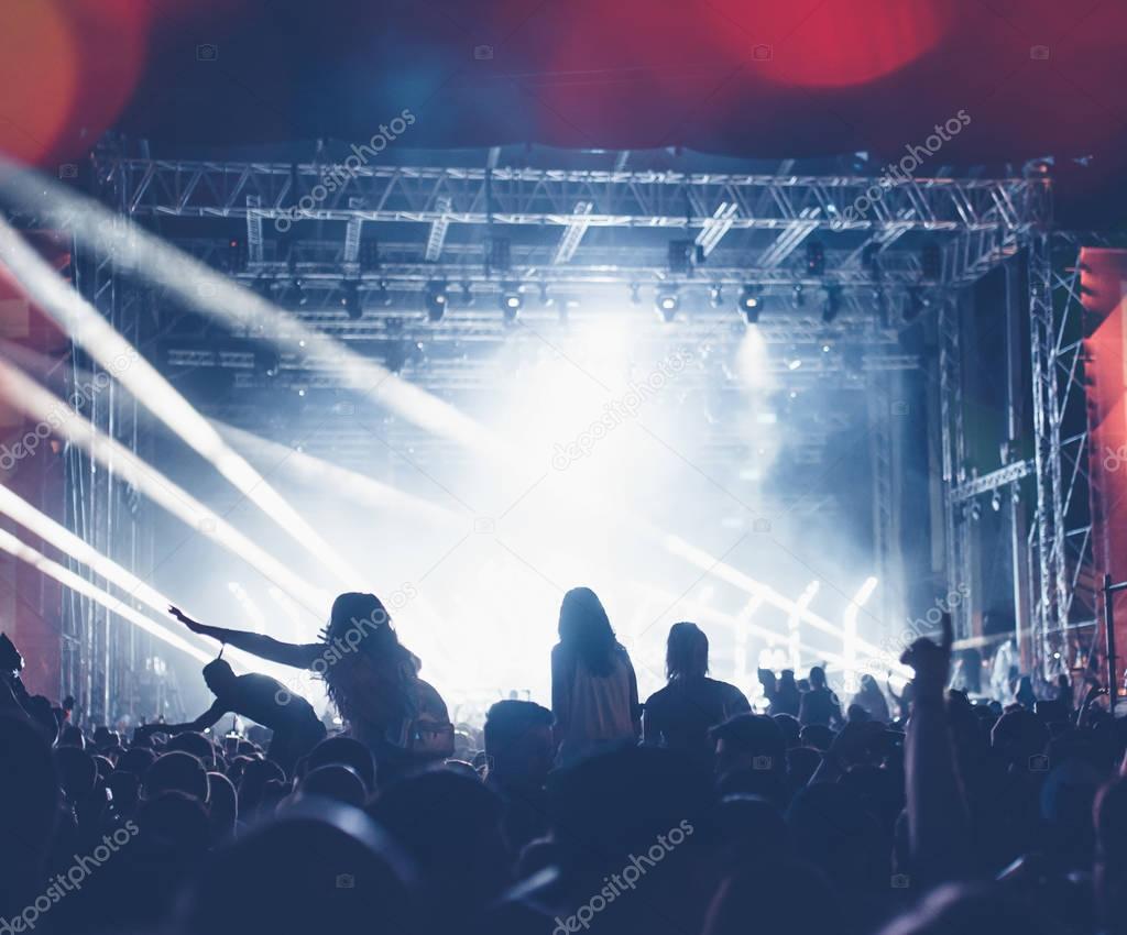 Silhouettes of festival concert crowd in front of bright stage lights. Unrecognizable people and colorful effects