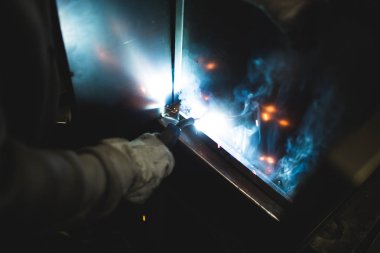 Metallurgy industry. Factory for production of heavy pellet stoves and boilers. Close up of manual worker welder on his job. Extremely dark conditions and visible noise clipart