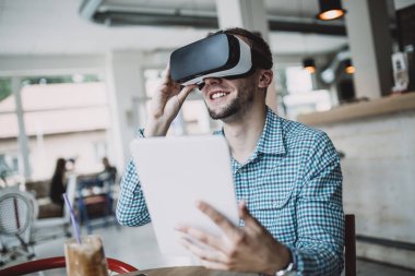 Cyber kafede oturan ve sanal gerçeklik kulaklık veya gözlük kullanma yakışıklı genç adam