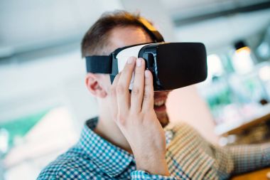 Cyber kafede oturan ve sanal gerçeklik kulaklık veya gözlük kullanma yakışıklı genç adam