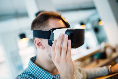 Cyber kafede oturan ve sanal gerçeklik kulaklık veya gözlük kullanma yakışıklı genç adam