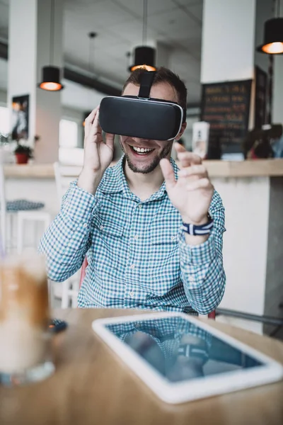 Cyber kafede oturan ve sanal gerçeklik kulaklık veya gözlük kullanma yakışıklı genç adam