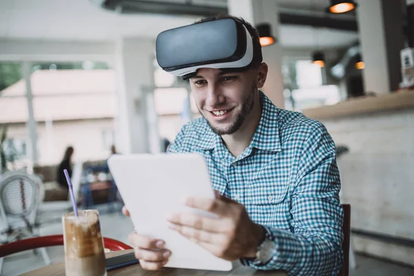 Young handsome man sitting in cyber cafe and using virtual reality headset or glasses