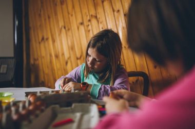 Paskalya tatil keyfini iki kız. Onlar boyama ve yumurta dekorasyon mutfak masasına oturuyorlar