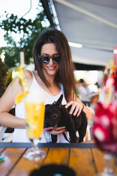 Beautiful young woman with sunglasses sitting in cafe with her adorable French bulldog puppy. People with dogs theme