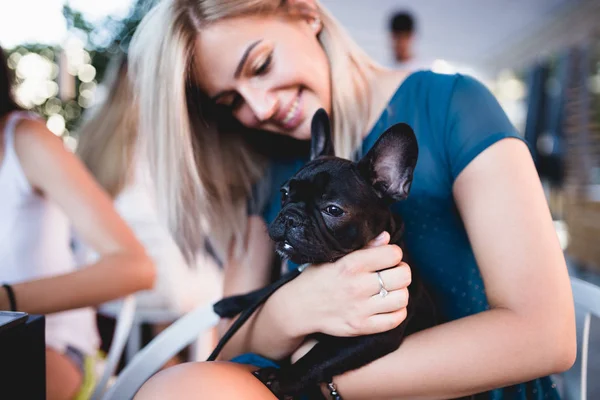Beautiful young blonde woman enjoying with her french bulldog puppy in cafe bar