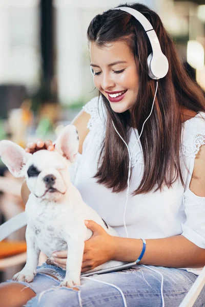 Beautiful young woman sitting in cafe with her adorable French bulldog puppy. Spring or summer city outdoors. People with dogs theme