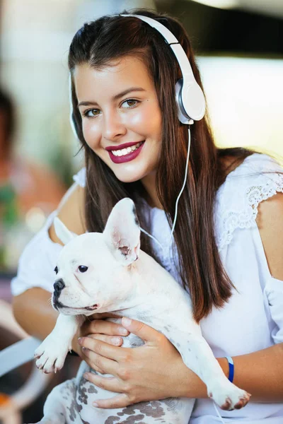 Beautiful young woman sitting in cafe with her adorable French bulldog puppy. Spring or summer city outdoors. People with dogs theme