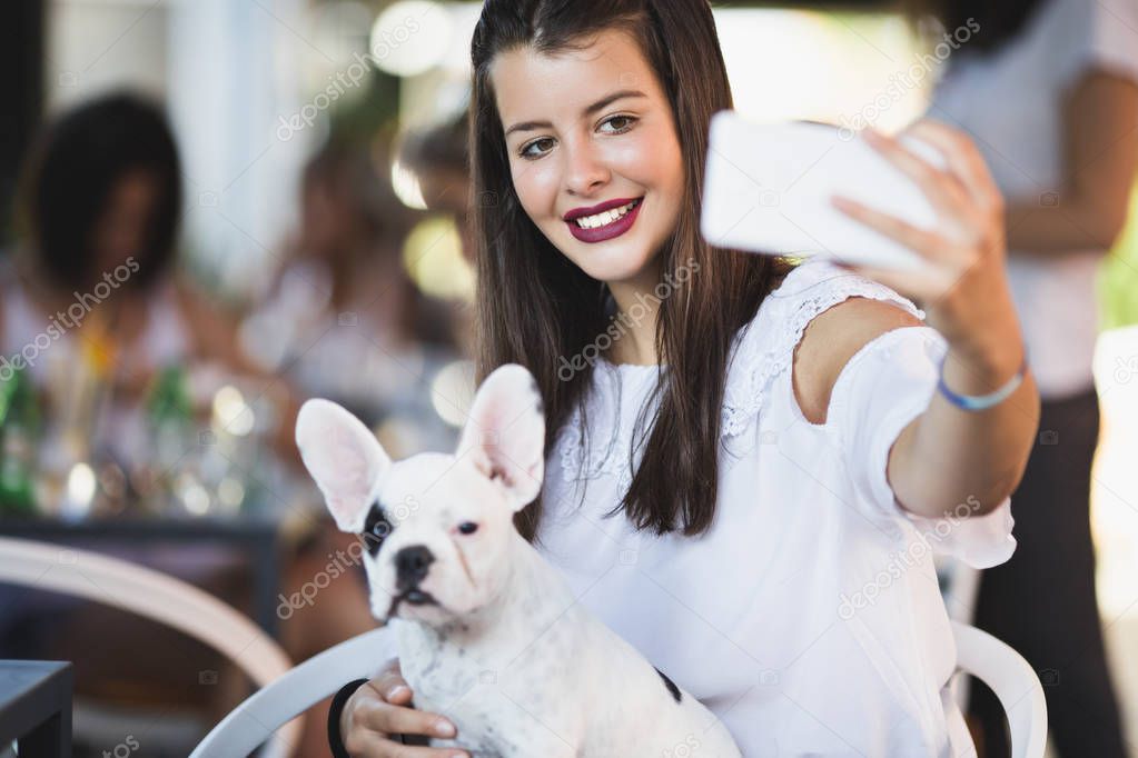 Beautiful young woman sitting in cafe with her adorable French bulldog puppy. Spring or summer city outdoors. People with dogs theme