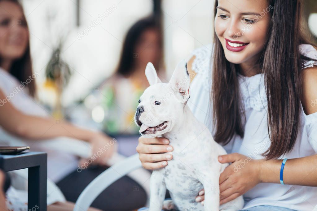 Beautiful young woman sitting in cafe with her adorable French bulldog puppy. People with dogs theme