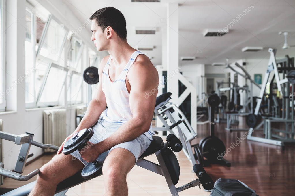 Young attractive adult man exercising and doing weight lifting at fitness gym. Sport training indoors