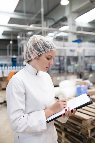 Young woman worker checking robotic line for bottling and packaging pure drinking water into bottles and canisters