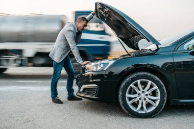 Orta yaşlı şık bir işadamı araba arızasını veya motor arızasını düzeltmeye çalışıyor ve yolda araba kazası için çekici servisi bekliyor. Yol kenarı yardım kavramı.