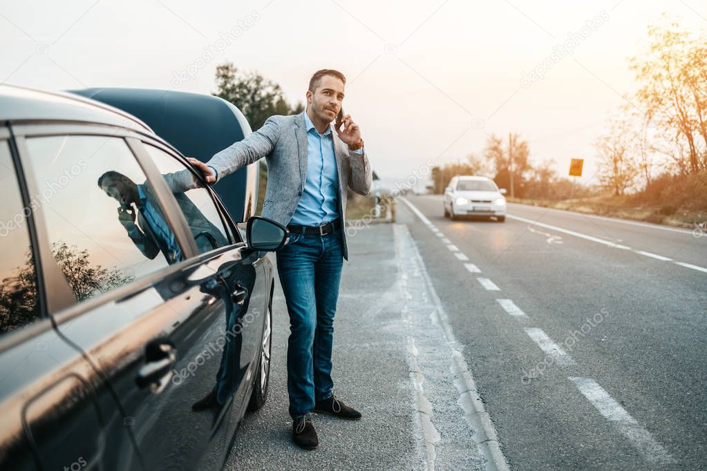 Elegant middle age business man calling towing service for help on the road. Roadside assistance concept.