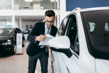 Galeride çalışan araba satıcısı ve araba detaylarını son kez kontrol ediyor alıcı gelmeden önce..