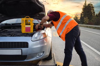 Çekici servisinde çalışan yol asistanı atlama marşı ve hava kompresörlü enerji istasyonuyla araba motorunu çalıştırmaya çalışıyor. Yol kenarı yardım kavramı.